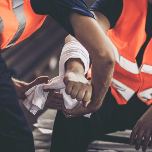 Close up of unrecognizable manual worker assisting his colleague with physical injury in steel mill.